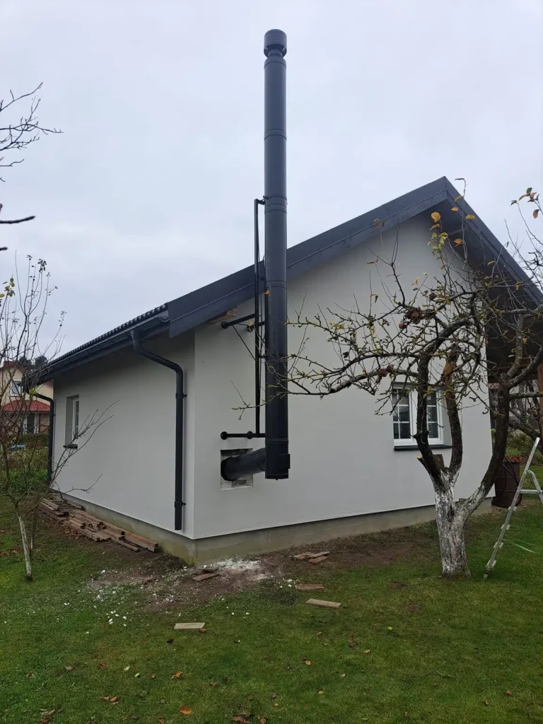 Baltas pastatas su juodu kamino vamzdžiu, pritvirtintu prie šono. Pastatas turi baltą langą.