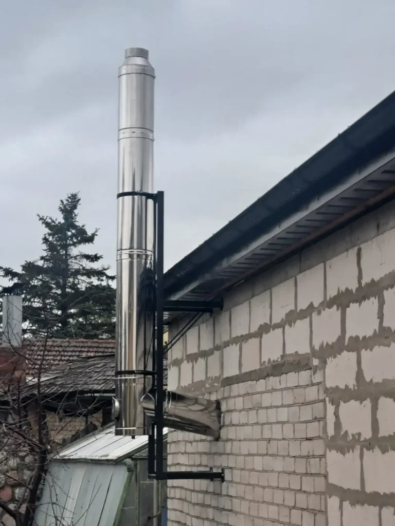 Aukšto, sidabrinio kamino stambus planas debesuoto pilko dangaus fone.